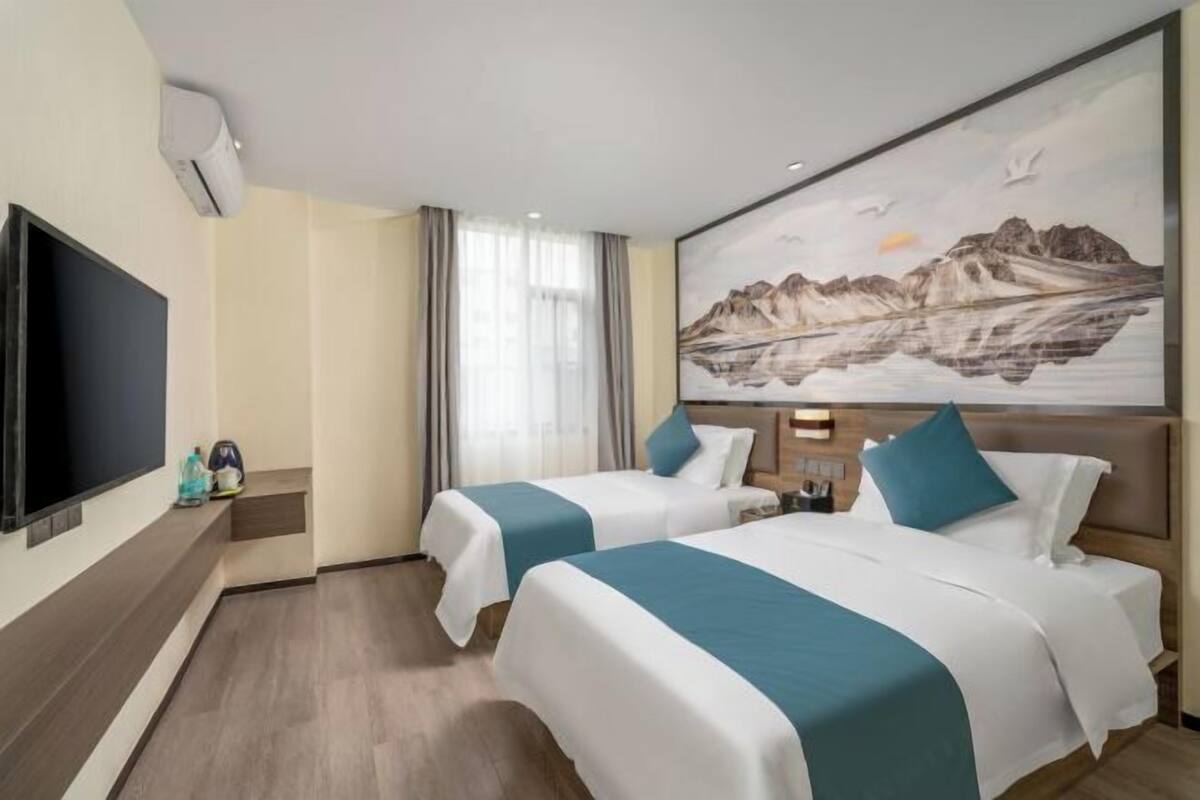 Habitación de hotel con dos camas, un televisor de pantalla plana, un cuadro de montañas y una ventana con cortinas.