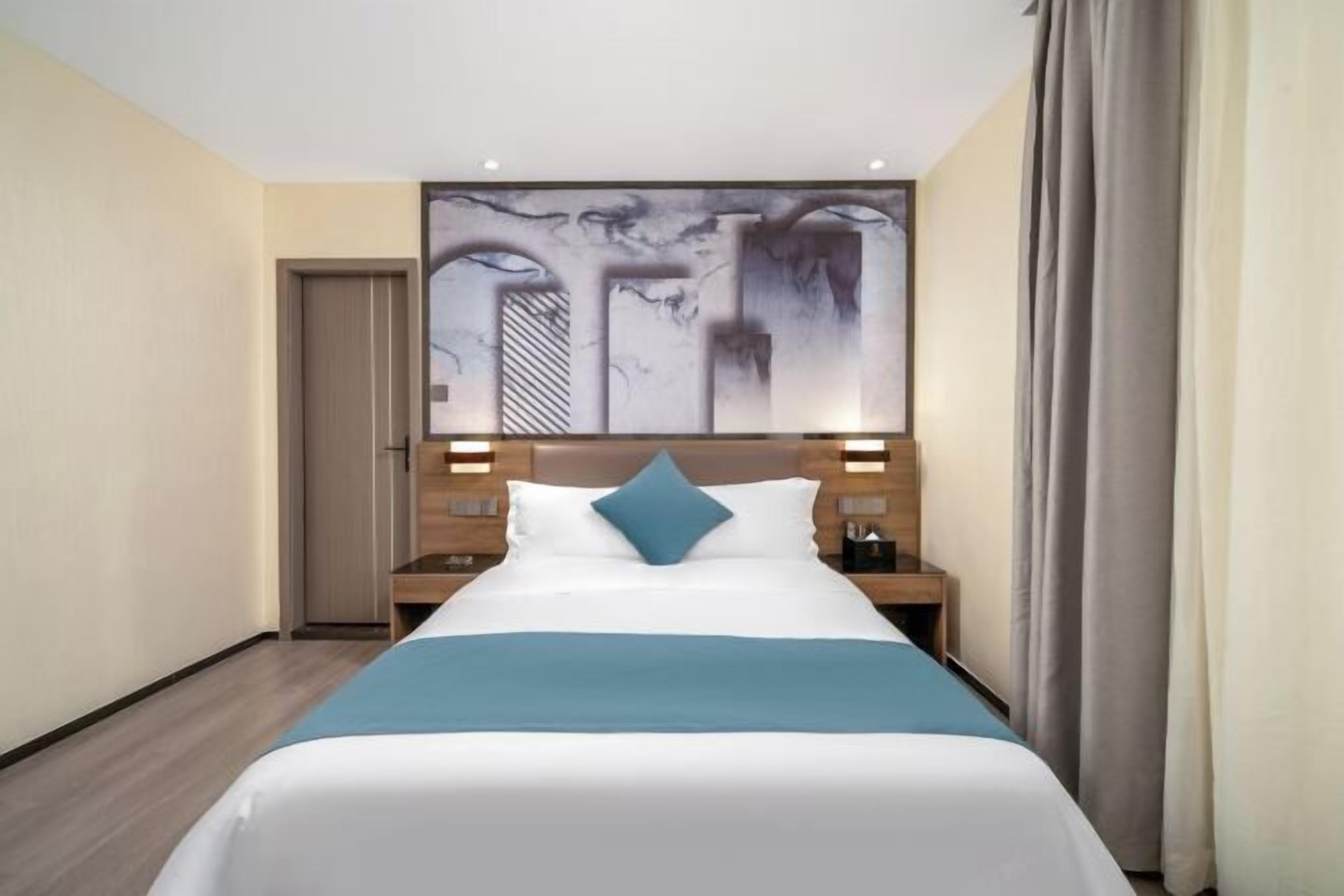 A hotel room with a bed, a headboard with a painting, a nightstand, and a door.