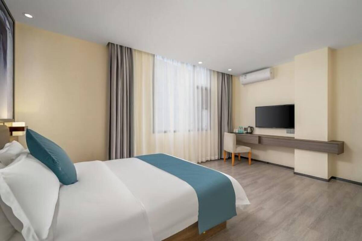 Una habitación de hotel con cama, escritorio, televisor y ventana con cortinas.