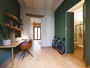 A room with a wooden desk, a chair, a potted plant, a bookshelf, a bicycle, and a door leading to a bathroom. - Bravissimo Estudi Verd; Spacious 3-bedroom apartment in the Historic Centre (Girona)