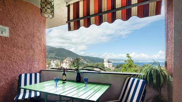 A balcony with a table and striped chairs, a bottle, and two glasses. - [Spacious +sea view with garden] (Arenzano)