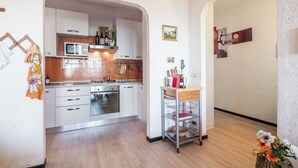 A compact kitchen with white cabinets, a microwave, stove, and oven. There is a small dining area with a table and chairs. - [Spacious +sea view with garden] (Arenzano)