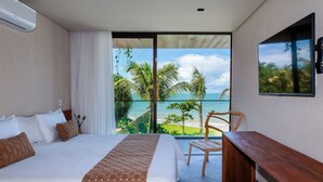 Una habitación de hotel con cama, escritorio de madera y ventana grande con vistas a la playa y palmeras.