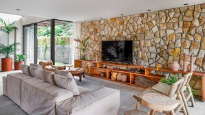 Una sala de estar moderna con una pared de piedra, un televisor grande, un sofá y una mesa de centro.