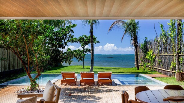 Zona de piscina con mobiliario de madera, vista al océano y vegetación tropical.