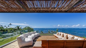 Una terraza de madera con un sofá blanco y un banco de madera, orientada hacia un océano azul y despejado.