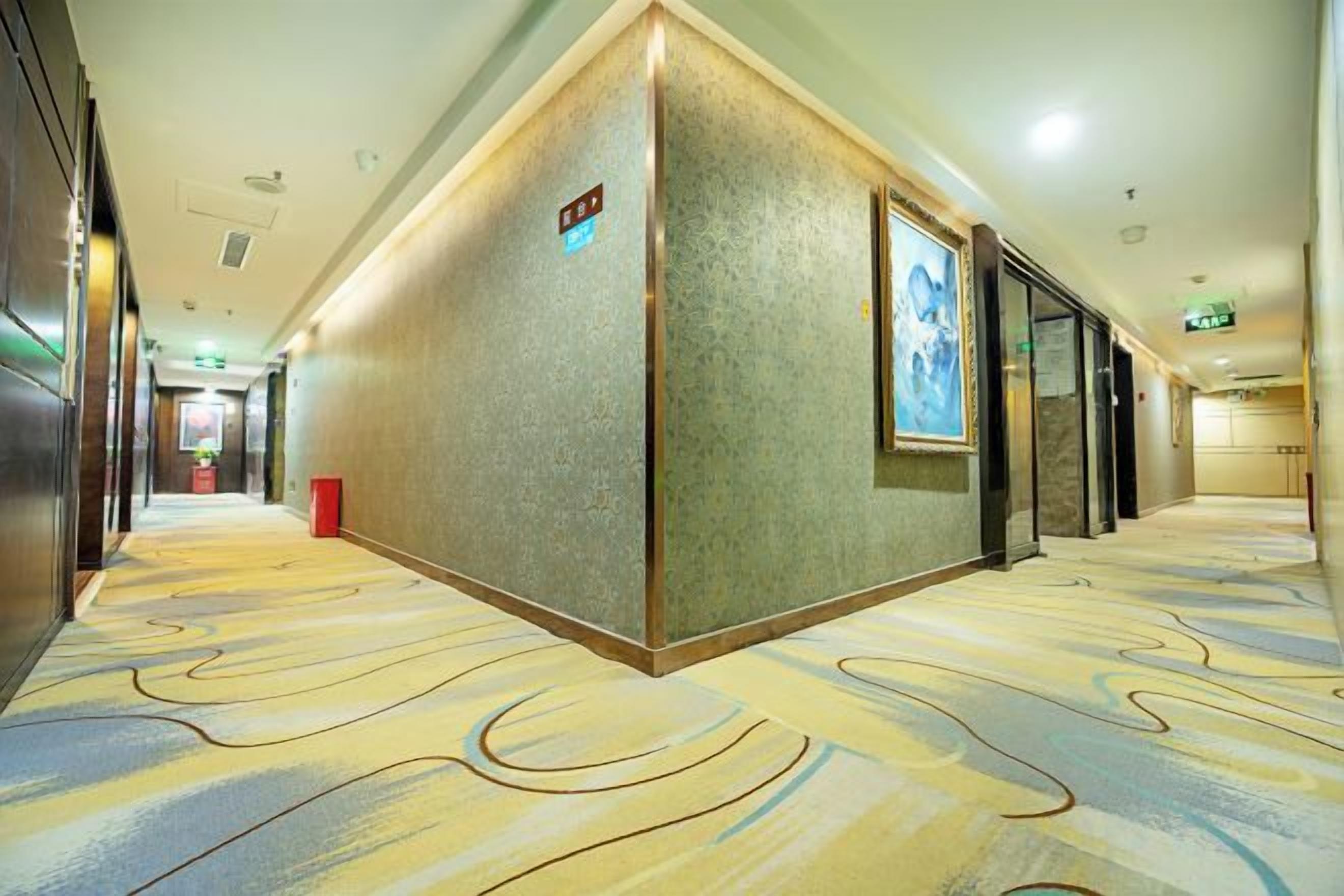 A hotel corridor with a patterned carpet, a reception desk, and a framed picture on the wall.