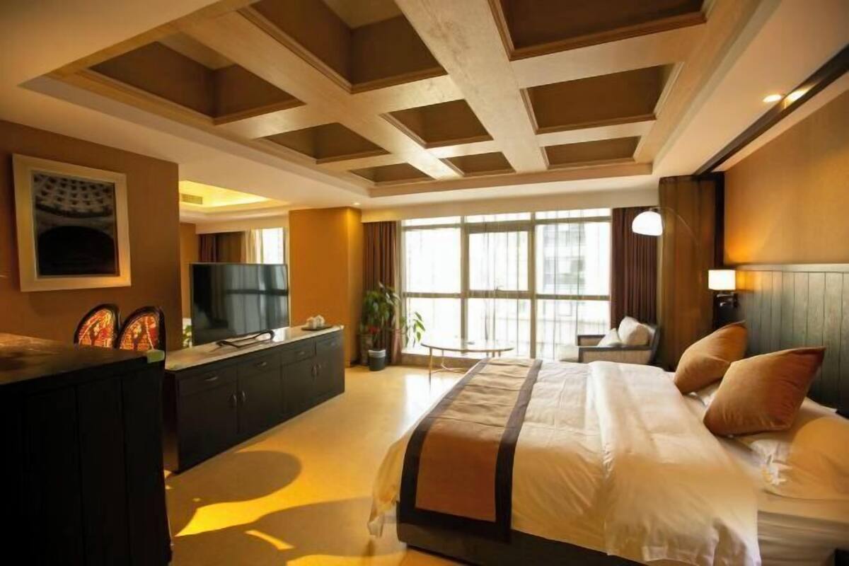 Une chambre d’hôtel avec un grand lit, un bureau avec une télévision, une fenêtre avec des rideaux et un plafond avec des poutres en bois.