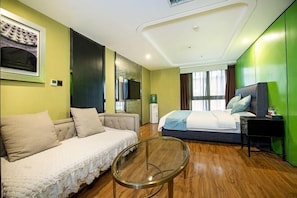 A modern hotel room with a sofa, a bed, a glass coffee table, and a television. - Yinggeli Hotel (Zhengzhou East Railway Station Convention and Exhibition Center) (Zhengzhou)