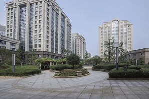 Une place urbaine moderne, bordĂ©e dâimmeubles de grande hauteur, agrĂ©mentĂ©e dâespaces verts bien entretenus et dotĂ©e dâune zone centrale circulaire.