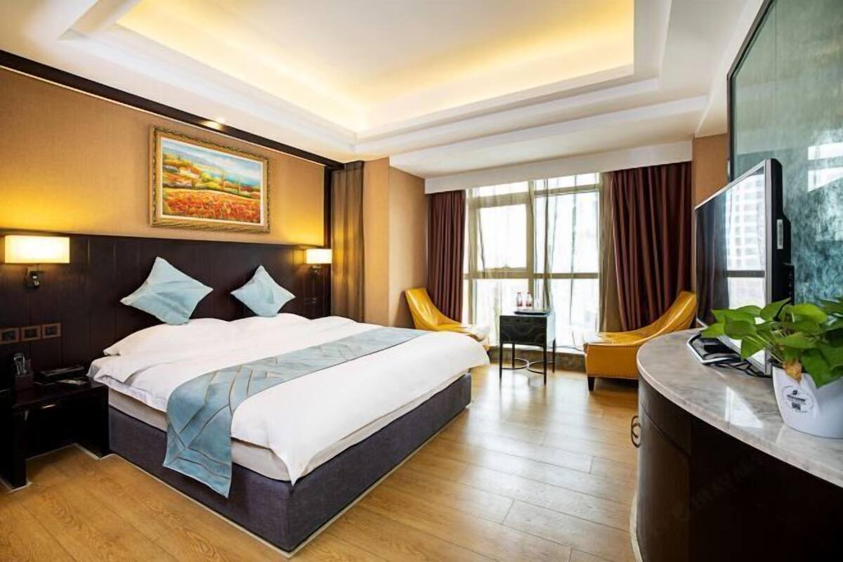 Une chambre d’hôtel comprenant un lit, des lampes de chevet, un bureau avec une chaise, une télévision et une grande fenêtre avec des rideaux.