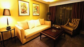 Ein Hotelzimmer mit Sofa, Ohrensessel, Couchtisch und zwei gerahmten Kunstwerken an der Wand.