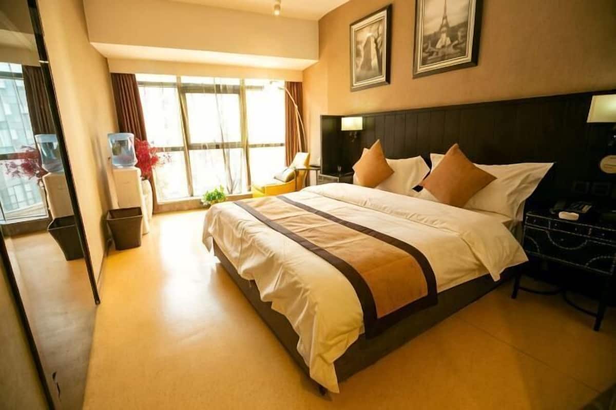 Une chambre d’hôtel avec un grand lit, un bureau, une chaise, une fenêtre avec des rideaux et un tableau encadré au mur.