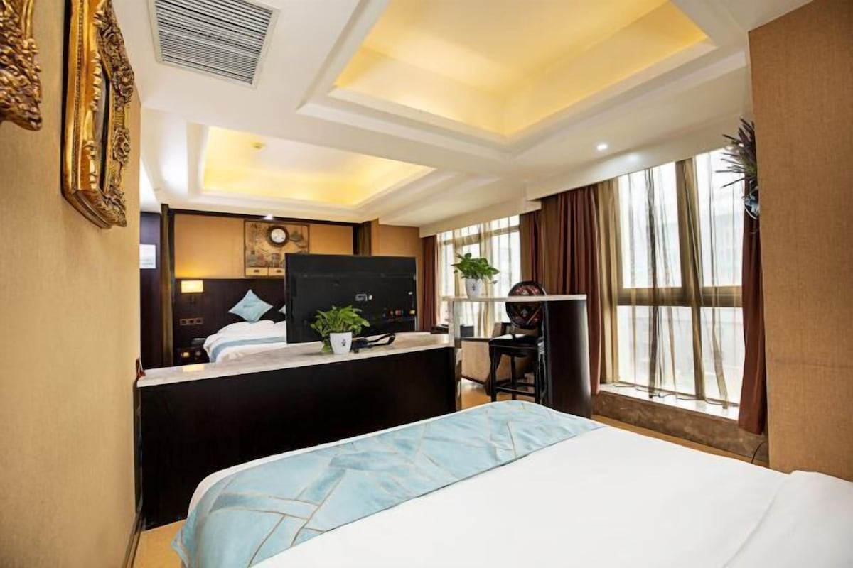 A hotel room with a bed, desk, chair, and large windows.