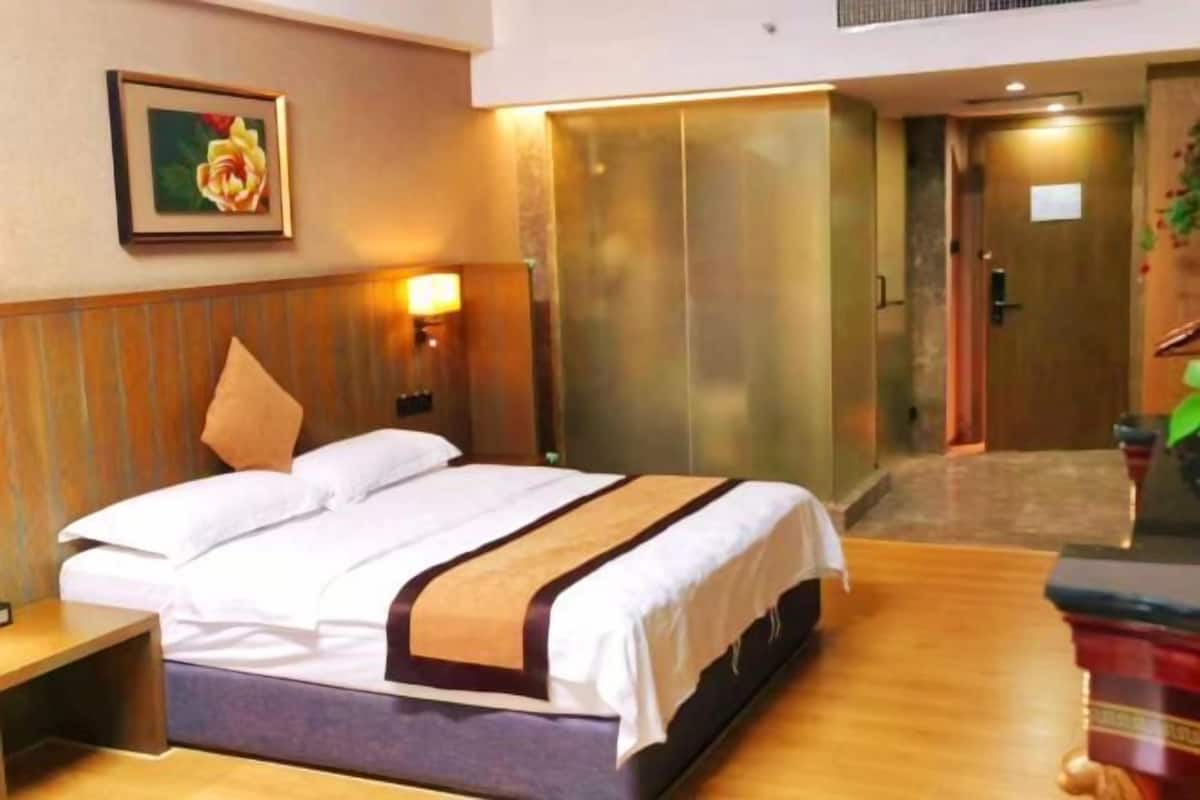 Une chambre d’hôtel comprenant un lit, une table de chevet, une lampe fixée au mur et une porte avec un panneau de verre.
