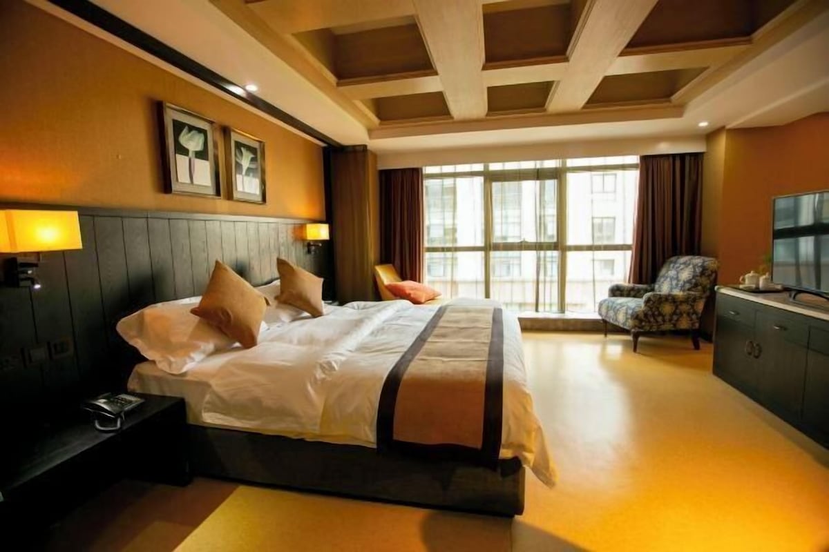 A hotel room with a large bed, a desk with a lamp, a chair, and a TV.