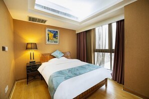 A hotel room with a large bed, a nightstand with a lamp, a painting on the wall, and a window with curtains.