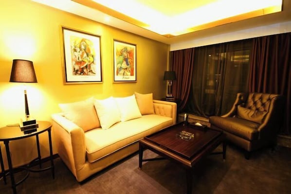 A hotel room with a sofa, armchair, coffee table, and two framed artworks on the wall. - Yinggeli Hotel (Zhengzhou East Railway Station Convention and Exhibition Center) (Zhengzhou)