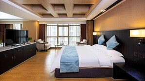 Ein Hotelzimmer mit einem großen Bett, einem Fernseher, einem Schreibtisch und Blick auf die Stadt durch große Fenster.