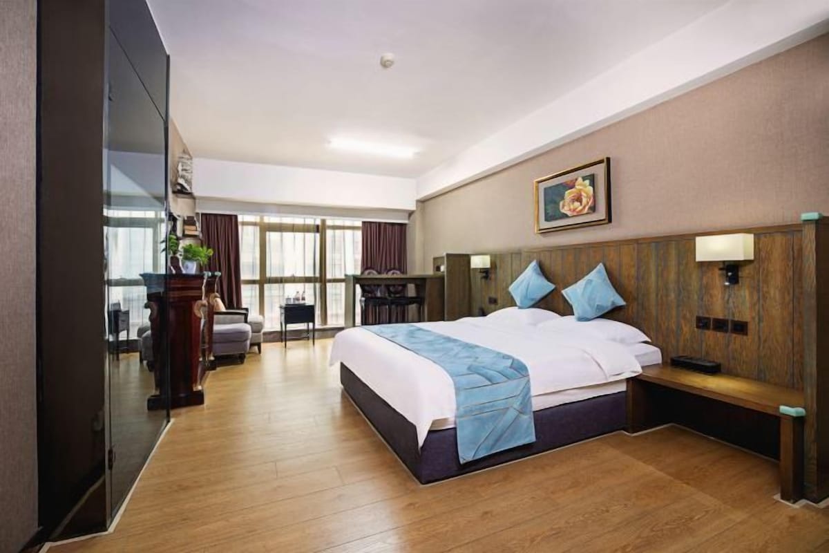 A hotel room with a large bed, a desk, a chair, and a view of the outdoors.