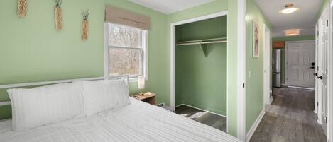 A bedroom with a bed, a nightstand, a window, a closet, and a hallway leading to a bathroom.