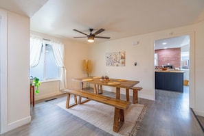 A dining area with a wooden table and benches, a ceiling fan, and a view into the kitchen.