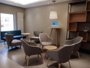 A modern lounge area with sofas and chairs, a coffee machine, and a laptop on a small table.
