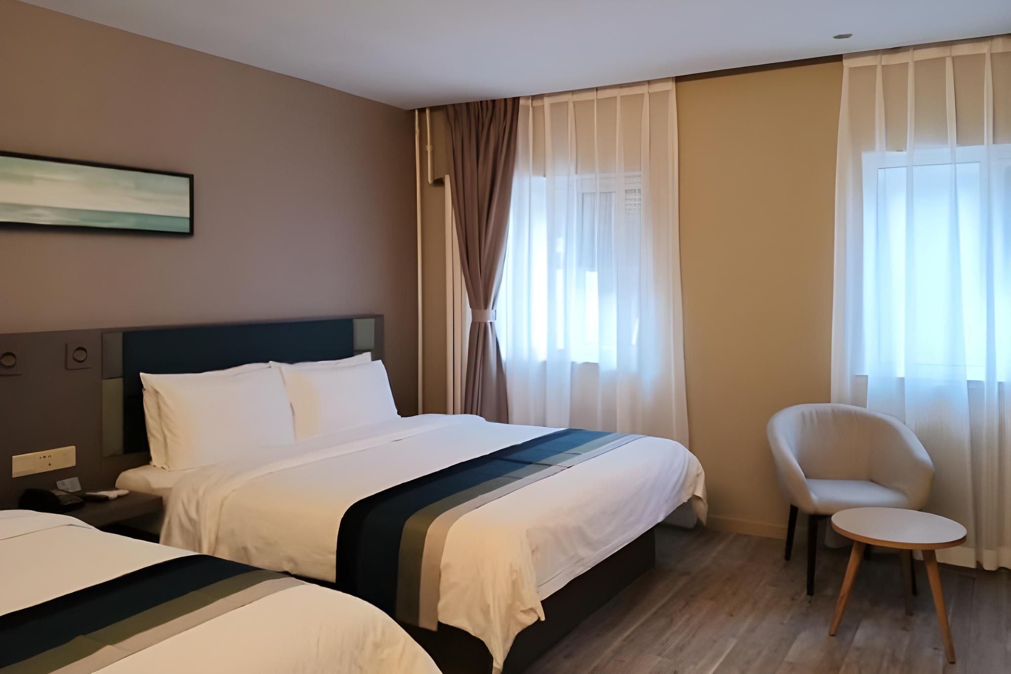 Une chambre d’hôtel avec deux lits, une chaise et un tableau au mur.