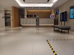 En hotellobby med reception, bænk og tydelig gulvbane.