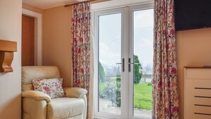 A room with a leather armchair, a wooden cabinet, and a sliding glass door leading to a garden. - 1 bedroom accommodation in Netherseal (Netherseal)