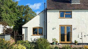 A two-story house with a white exterior, a chimney, and a wooden door. - 1 bedroom accommodation in Netherseal (Netherseal)