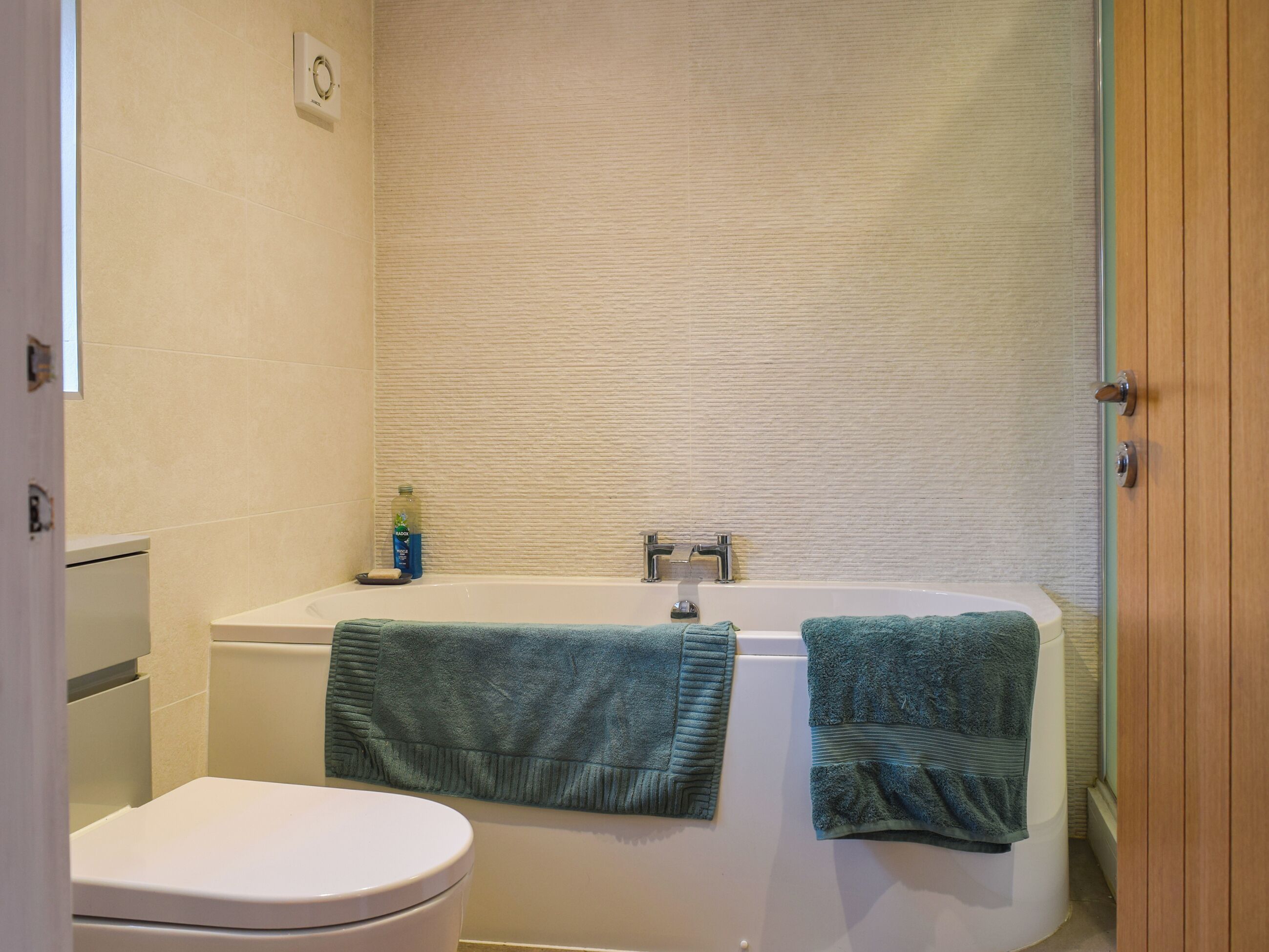 A bathroom with a white bathtub, a toilet, and two towels hanging on the wall.