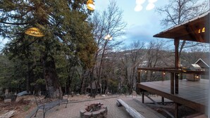 A wooden deck with a fire pit, benches, and a covered area with a grill.