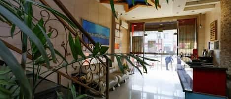 A hotel lobby with a reception desk, a staircase, and a large window.