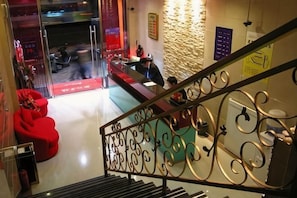 Un vestíbulo de hotel con una escalera, una mesa de recepción y un puerta de vidrio que da al exterior.