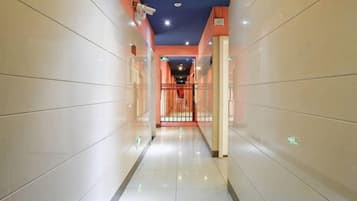 Un couloir au sol et aux murs carrelés, qui mène à une porte au fond.