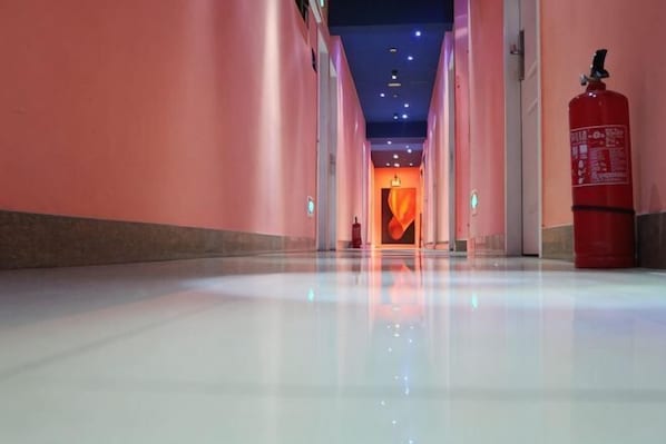 A corridor with a polished floor, a fire extinguisher, and a door at the end.