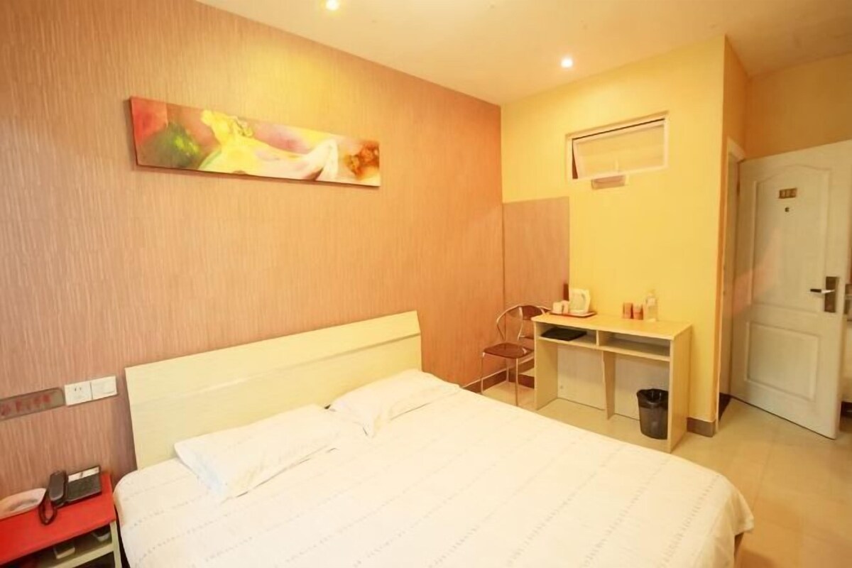 Een hotelkamer met een bed, een bureau, een stoel, een prullenbak en een deur.