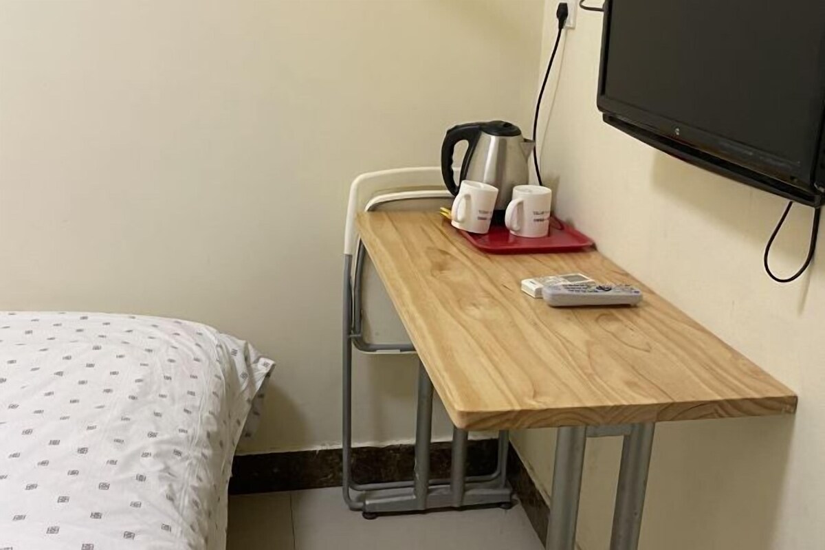 A small room with a bed, a wooden table with a kettle, cups, and a remote control.