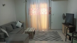 A living room with a sofa, a coffee table, a TV, and a patterned rug. - Cozy chalet in beautiful الغردقة with AC, WiFi, fitness room (الغردقة)