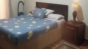 A bedroom with a bed, a nightstand, an air conditioner, a lamp, and a patterned rug. - Cozy chalet in beautiful الغردقة with AC, WiFi, fitness room (الغردقة)