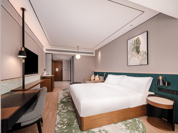 Ein modernes Hotelzimmer mit einem großen Bett, einem Schreibtisch mit Stuhl, einem Fernseher und einem Nachttisch mit Lampe.