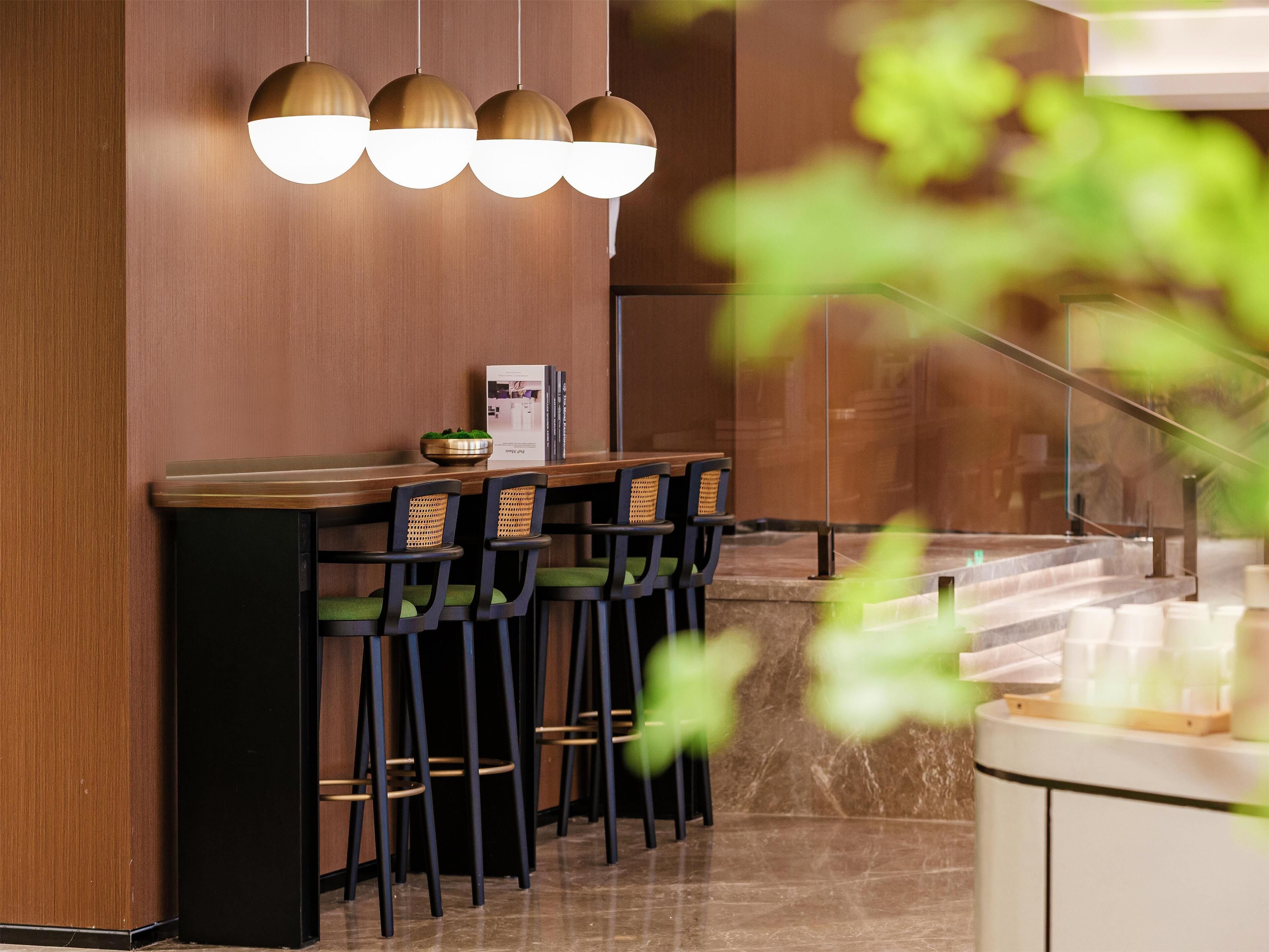 Zona de bar moderna con pared de madera, mostrador de mármol y sillas negras con cojines verdes.