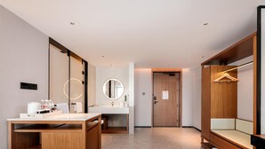A modern hotel bathroom with a wooden vanity, a round mirror, a sink, and a bench with a hanging rack. - Hilton Garden Inn Taiyuan Jiefang Road (Taiyuan)