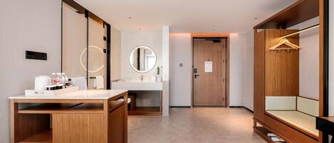 A modern hotel bathroom with a wooden vanity, a round mirror, a sink, and a bench with a hanging rack.