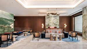 A modern hotel lobby with a high ceiling, recessed lighting, a large seating area with sofas and chairs, and a large window providing a view. - Hilton Garden Inn Taiyuan Jiefang Road (Taiyuan)