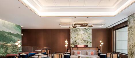 Un hall d’hôtel moderne avec un plafond haut, un éclairage encastré, un grand espace salon doté de canapés et de fauteuils, et une grande fenêtre offrant une vue.