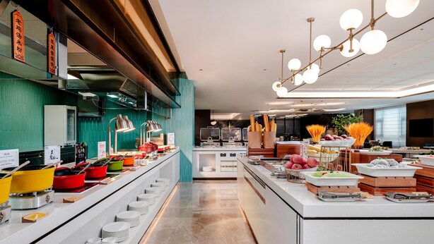 A modern kitchen with a central island, various cooking stations, and a seating area with a view of the city. - Hilton Garden Inn Taiyuan Jiefang Road (Taiyuan)