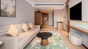 A modern hotel room with a sofa, a coffee table, a TV mounted on the wall, and a hallway leading to another room. - Hilton Garden Inn Taiyuan Jiefang Road (Taiyuan)
