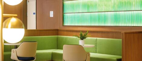 A reception area with a green sofa, two chairs, a potted plant, and a wooden panel wall with a green striped window.